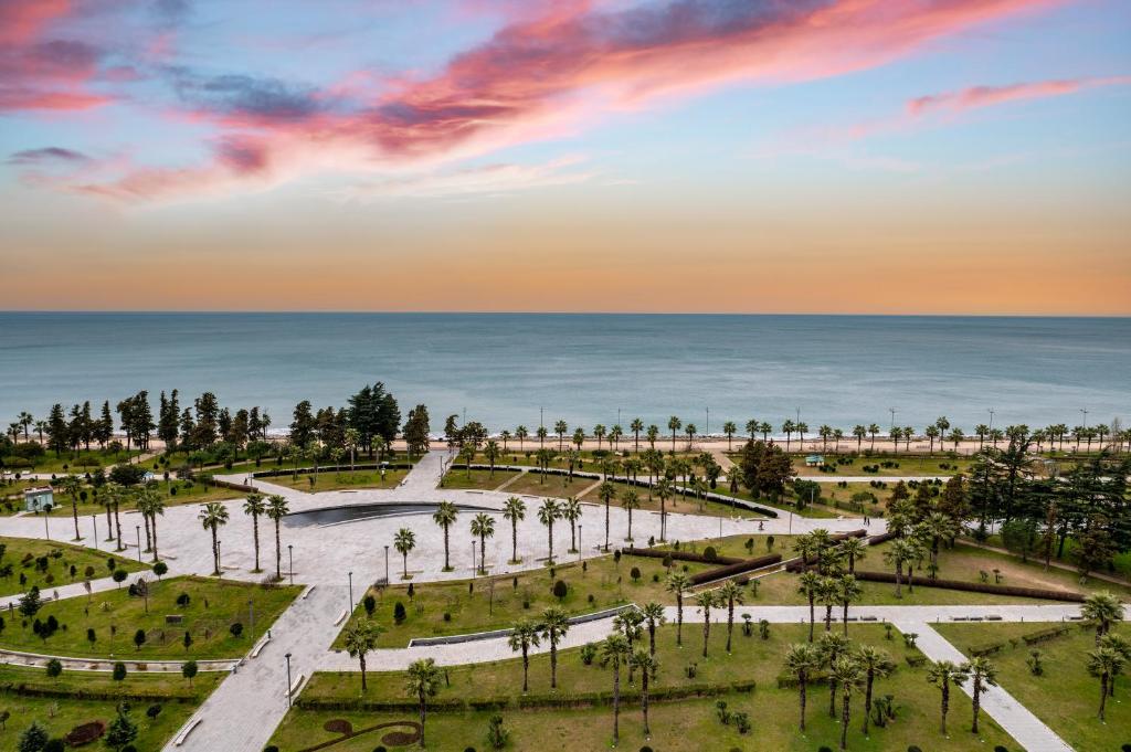 Skaista pludmales ainava ar palmu alejām un mierīgu jūru, kas apvīta ar krāšņām debesu krāsām saulrieta gaismā.