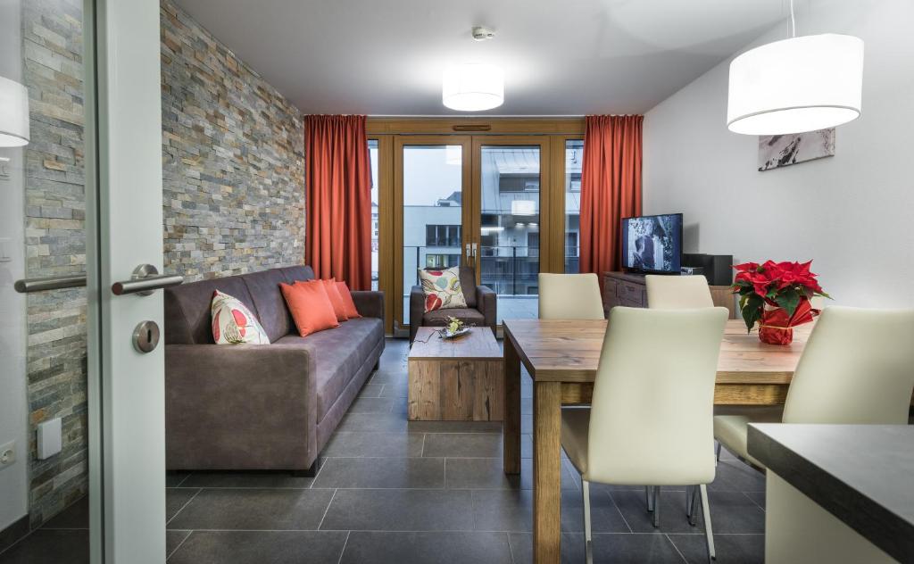 Mūsdienīga viesistaba ar akmens sienu, dīvānu un ēdamgaldu, dekorēta ar sarkanām aizkariem un ziediem. Gaisma rada siltu atmosfēru.