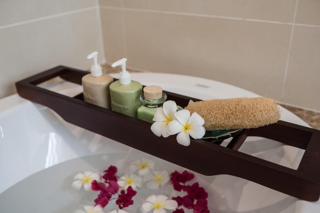 Vannas istabā esoša koka plaukta ar šampūnu, dušas želeju un sūkli, rotāts ar ziediem uz ūdens virsmas.