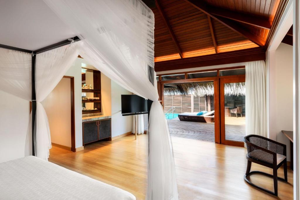 Mūsdienīga guļamistaba ar atvērtiem logiem, kas ved uz terasi ar baseinu, un elegantu dizainu, kurā ir gultas baldahīns un koka grīda.