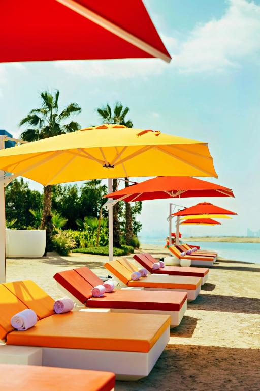 Voco Monaco Dubai pludmales sauļošanās krēsli zem košiem saulessargiem