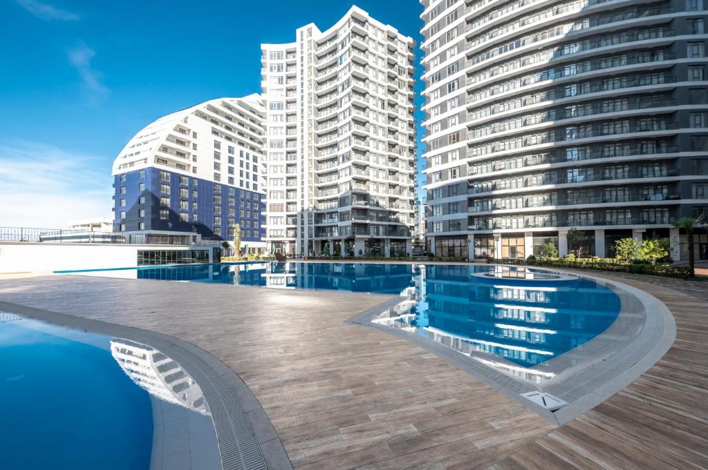 Mūsdienīgs dzīvokļu komplekss ar plašu baseinu un modernu arhitektūru, kas atspoguļojas ūdenī. Skaists skats uz debesīm un apzaļumotu apkārtni.
