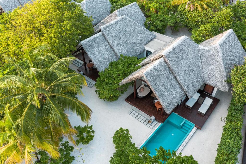 Tropu kūrorta villas ar salmu jumtiem un privātu peldbaseinu, ieskautas zaļo koku un palmām, radot mierīgu un eksotisku atmosfēru.
