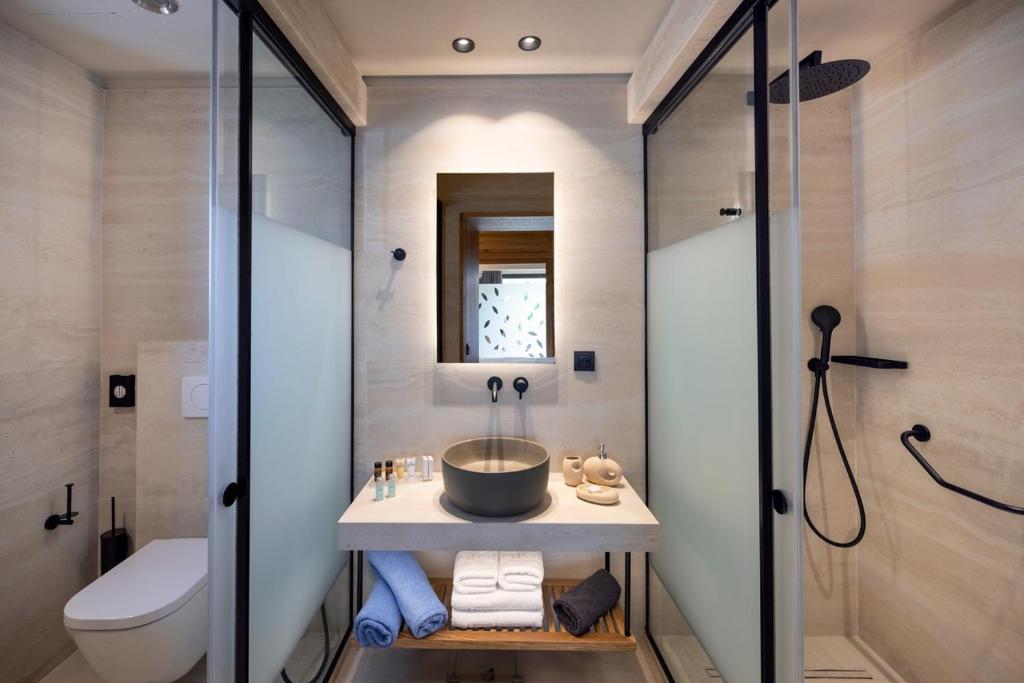 Moderns vannas istabas interjers ar stikla sienām, elegantu izlietni un vannas piederumiem uz plaukta. Svaigs un minimālisks dizains rada relaksējošu atmosfēru.