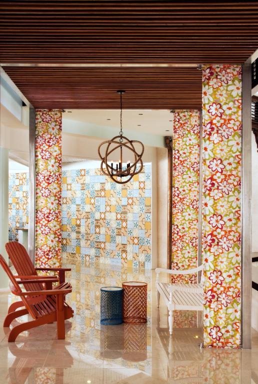 Skaista interjera aina ar krāsainām sienām un dekoratīviem kolonnām, kurās redzami ziedu raksti. Telpā ir koka griesti un stilīgi mēbeļu gabali, tostarp ērta sarkanā krēsla un divas krāsainas tvertnes.