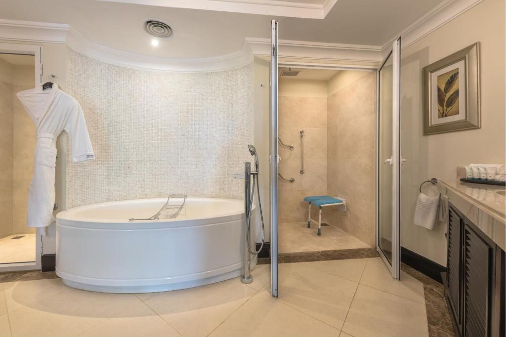 Mūsdienīga vannas istaba ar apaļu vannu un dušu, kurā ir pieejama sēdoša vieta, kā arī balta dvieļu drēbju komplekts. Eleganta interjera dizaina elementi un dabīgas krāsas rada relaksējošu atmosfēru.