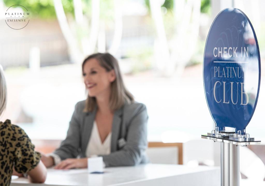 Reģistrācijas galds Platinum Club, kur profesionāla darbiniece apkalpo apmeklētāju. Attēlā redzama interjera telpa ar gaišiem toņiem un modernu dizainu.