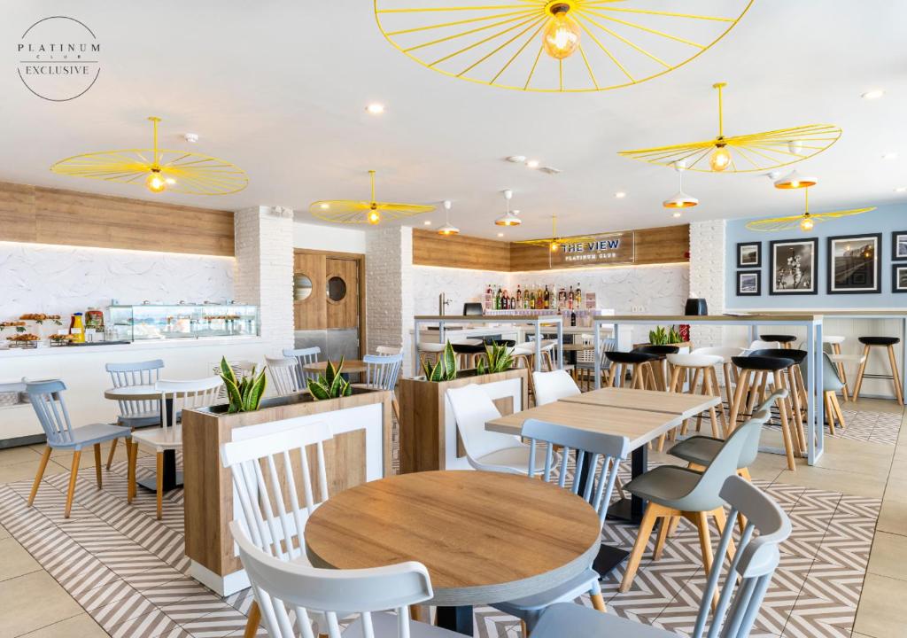 Mūsdienīgs kafejnīcas interjers ar dzelteniem griestu ventilatoriem, koka mēbelēm un izsmalcinātu apgaismojumu, radot patīkamu atmosfēru. 