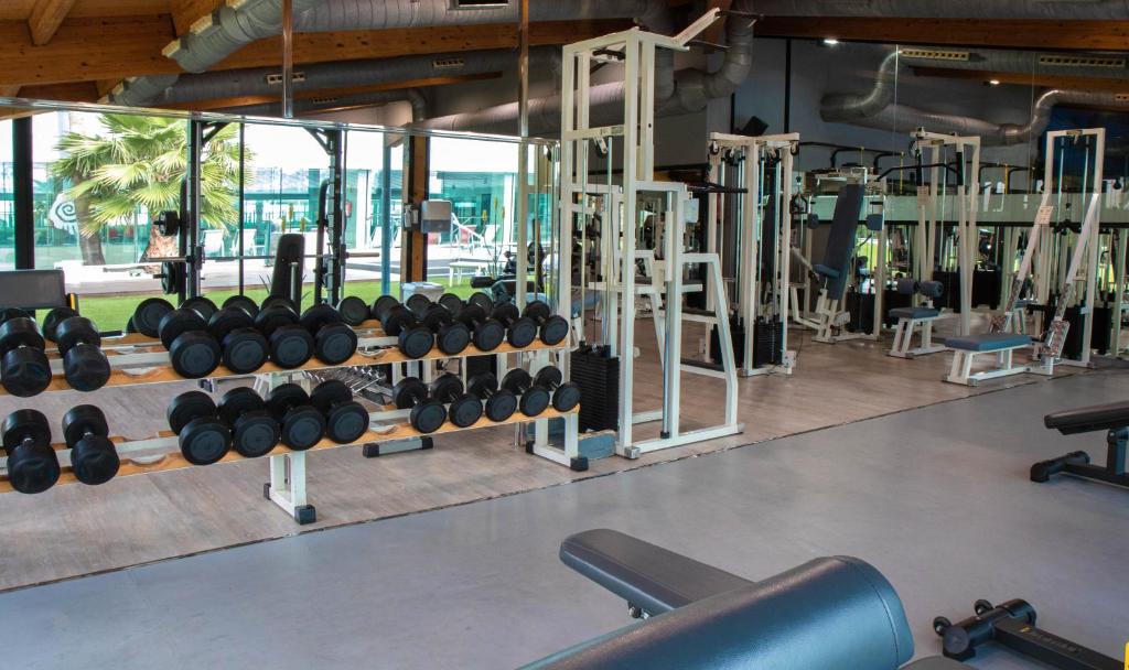 Sporta zāle ar dažādiem svara trenažieriem un hantelēm, kas ir sakārtoti uz plaukta. Gaisma ieplūst no logiem, radot patīkamu un motivējošu vidi treniņiem.