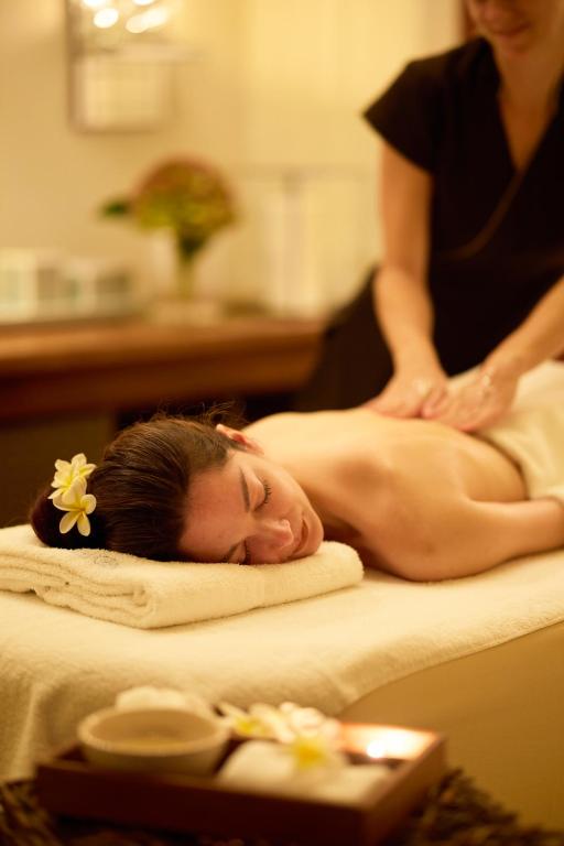 Sieviete saņem relaksējošu masāžu spa vidē, ar ziedu ornamentu matos. Apmēram ir redzami relaksācijas piederumi un svece.