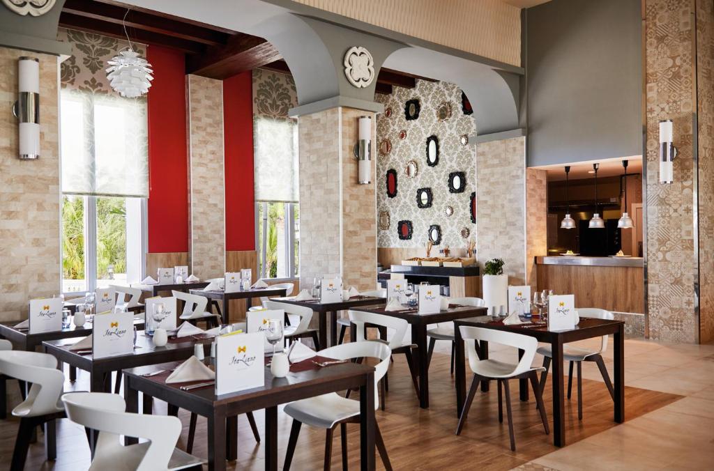 Mūsdienīgs restorāns ar elegantu interjeru, kur galdos novietoti ēdienkartes un dekoratīvi elementi. Gaismas un krāsu kombinācija rada patīkamu atmosfēru.