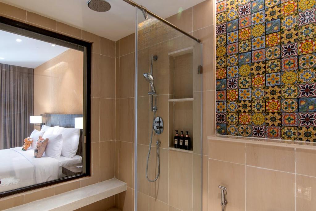 Mūsdienīgas vannas istabas interjers ar dušu un krāsainām flīzēm, redzams arī guļamistaba ar gultu un mīkstajām rotaļlietām.