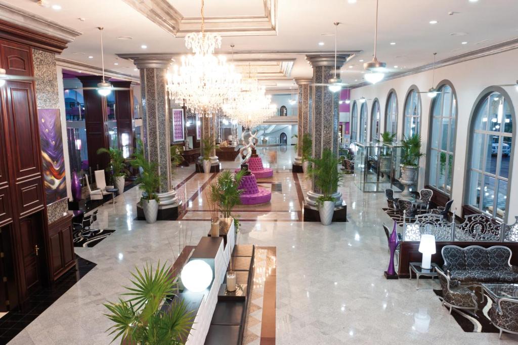 Mūsdienīga viesnīcas uzgaidāmā telpa ar elegantu dizainu, greznu apgaismojumu un zaļo augu akcentiem. Telpā ir izsmalcināti mēbeļu elementi un plašas logu vitrīnas.