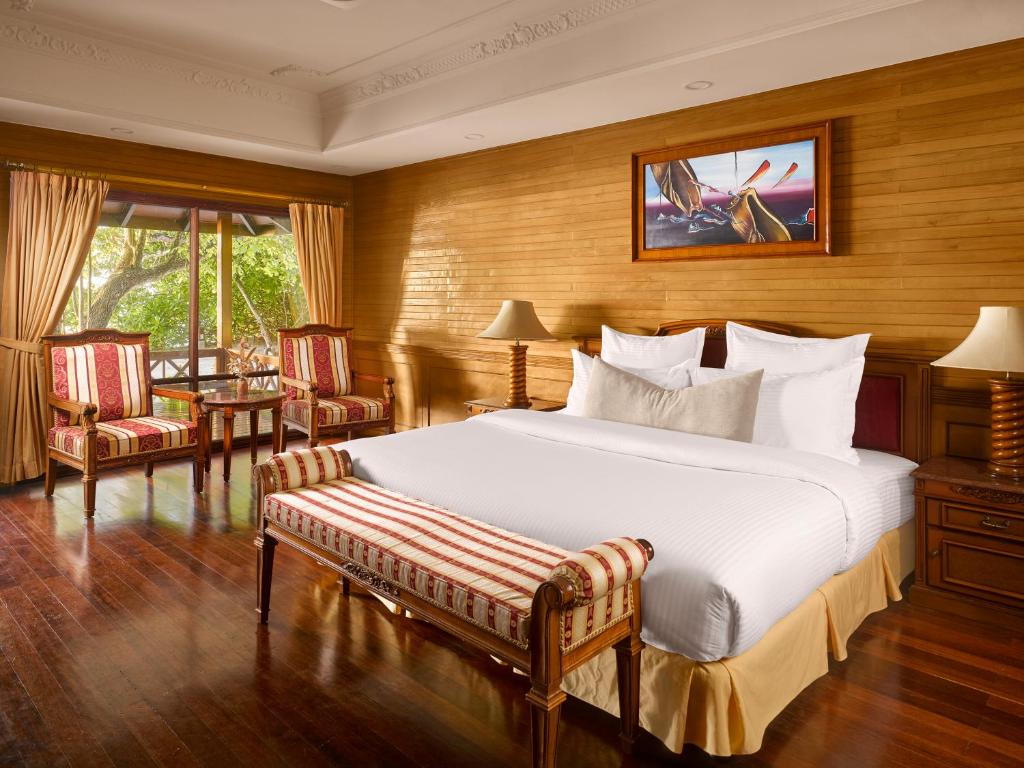 Mūsdienīgs guļamistabas interjers ar koka sienām, plašu gultu un dekoratīvu gultas soli. Telpā ir divas ērtas krēslus un galdiņš, kas aicina relaksēties pie loga ar skatu uz dārzu.