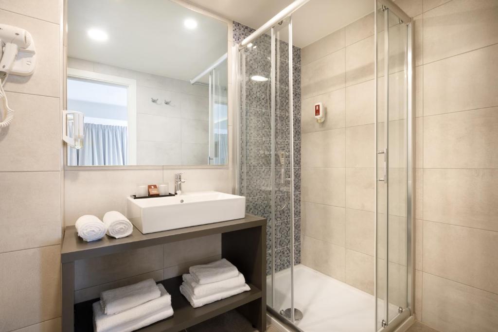 Mūsdienīgs vannas istabas interjers ar stikla dušu, izsmalcinātu izlietni un tīrām dvieļu kaudzēm. Vannas istaba ir gaiša un eleganta, radot komfortablu atmosfēru.