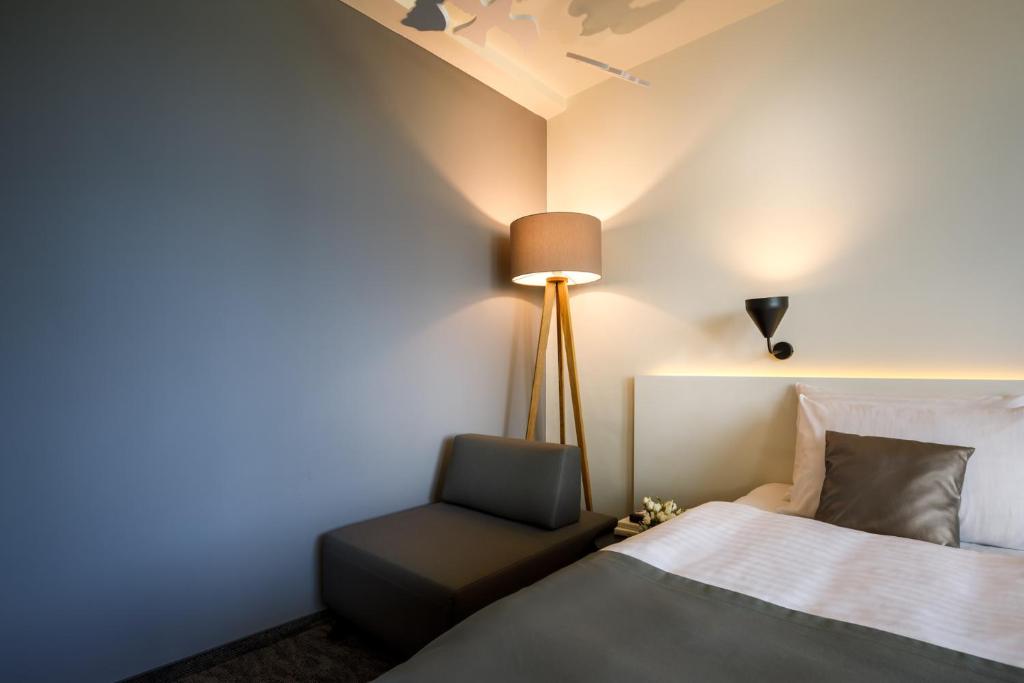 Mūsdienīga guļamistaba ar ērtu gultu un stilīgu apgaismojumu, kas rada mierīgu atmosfēru. Telpā ir pelēka siena un minimālisma dizains, kas piešķir eleganci.