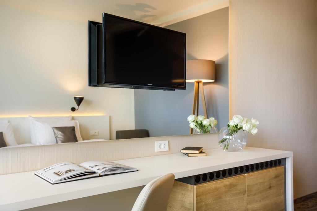 Mūsdienīgs viesnīcas numurs ar televizoru, rakstāmgaldu un dekoratīvām ziedu kompozīcijām. Elegantā interjerā ir gaiši toņi un mūsdienīgas mēbeles.