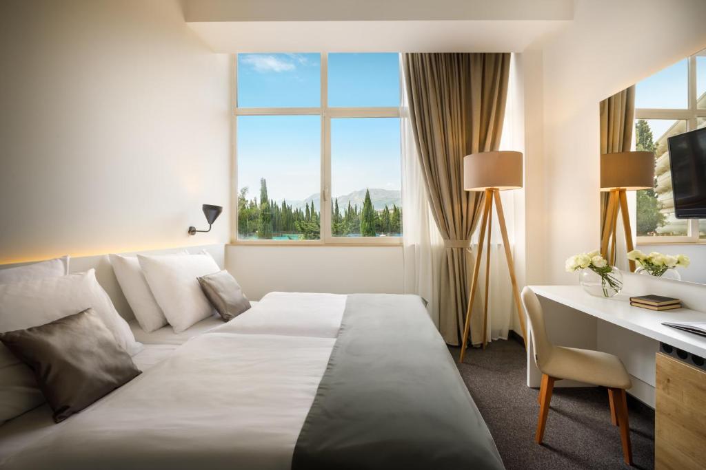 Mūsdienīgs viesnīcas numurs ar plašu logu, kas sniedz skatu uz dabu. Interjers ir gaišs un elegants, ar ērtiem gultas veļas komplektiem un stilīgu darba vietu.