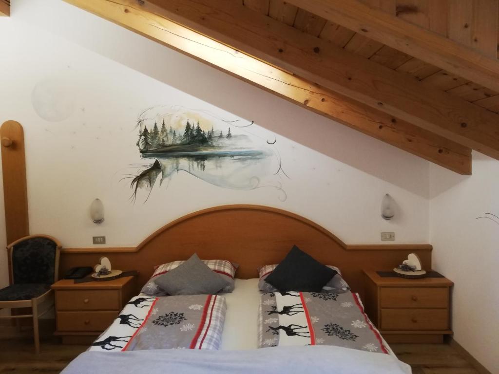 Mūsdienīga guļamistaba ar koka griestiem, dekorēta ar ainavu gleznu uz sienas un elegantiem gultas veļas komplektiem. Interjerā ir koka mēbeles un siltas krāsas, radot mājīgu atmosfēru.