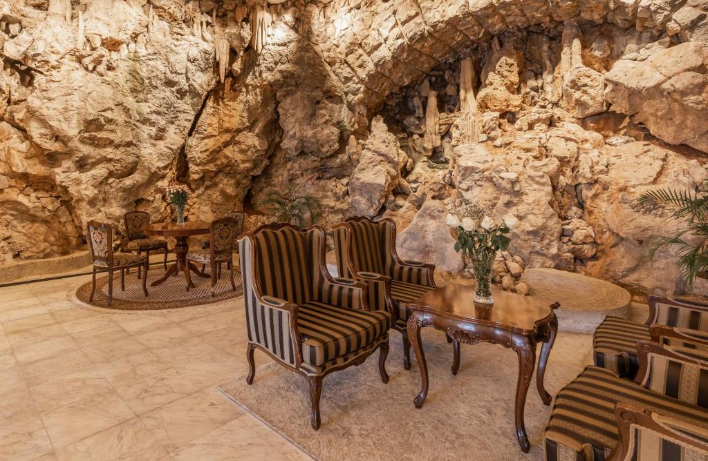 Eleganta atpūtas zona ar stilizētiem krēsliem un galdu, kas izvietota pret dabīgu akmens sienu. Iekārtojums apvieno greznību un dabu, radot harmonisku atmosfēru.