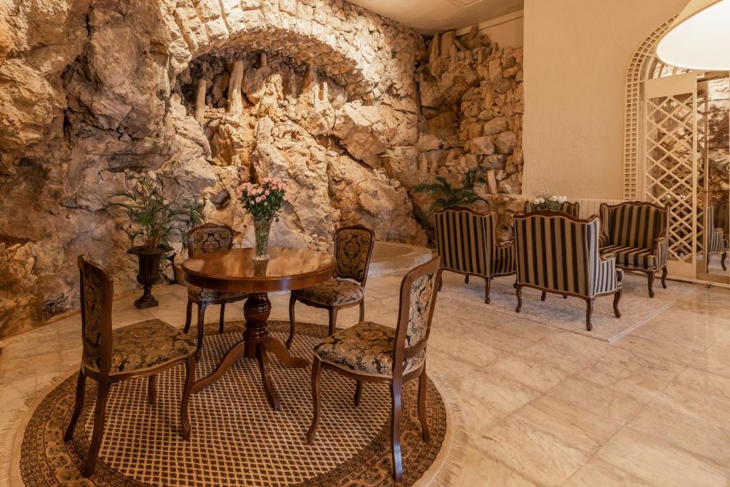 Eleganta atpūtas zona ar koka galdu un krēslu komplektu, ko ieskauj dabīgas akmens sienas un zaļumi, radot mierīgu atmosfēru.