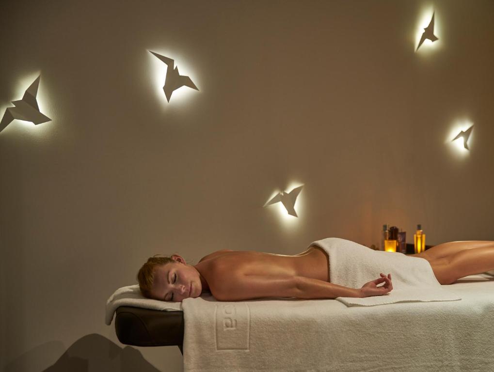 Relaksējoša spa procedūra ar apgaismotām origami putnu formām uz sienas un aromātiskiem eļļām blakus.