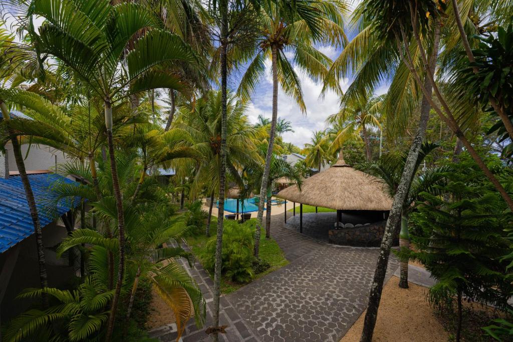 Tropu ainava ar palmām un atpūtas zonu, kurā redzama peldbaseina zona un tradicionāla jumta nojume. Ideāla vieta relaksācijai un atpūtai brīvā dabā.