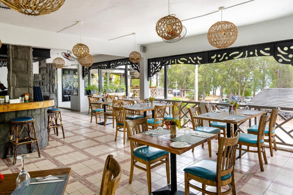 Mūsdienīga restorāna iekārtojums ar koka galdiem un krēsliem, rotātiem ar stilizētām lampām. Logi atveras uz zaļo dabu, radot patīkamu atmosfēru.