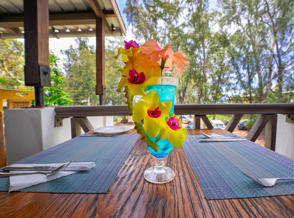 Krāsains kokteilis ar ziediem, novietots uz galda ārā, ar zaļumu fona ainavu. Ideāla vieta relaksācijai un baudīšanai.