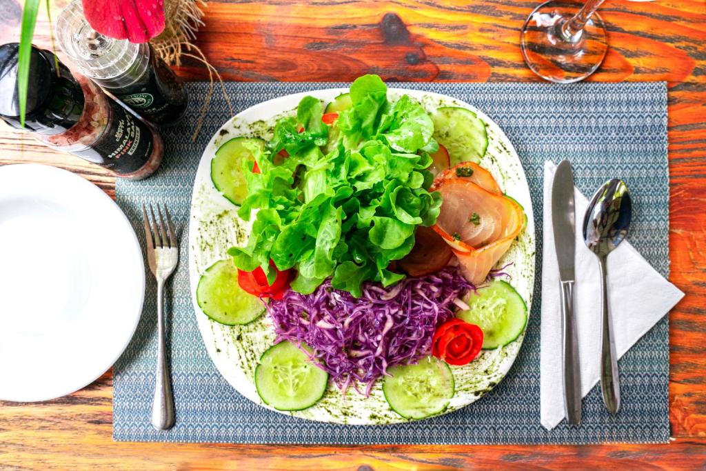 Svaiga dārzeņu salātu šķīvis ar salātu lapām, tomātiem, gurķiem un puravu, pasniegts uz galda ar galda piederumiem un garšvielām.