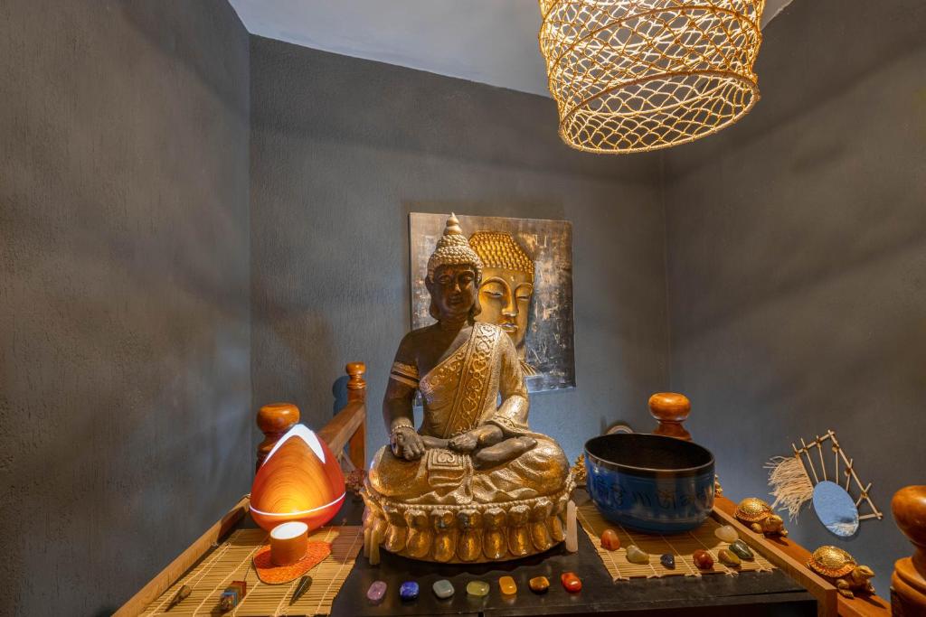 Meditatīvas telpas interjers ar zelta Budas statuju, akmens kristāliem un tradicionālajiem rīkiem, radot mierīgu atmosfēru. Gaismas avots papildina relaksējošo noskaņu.
