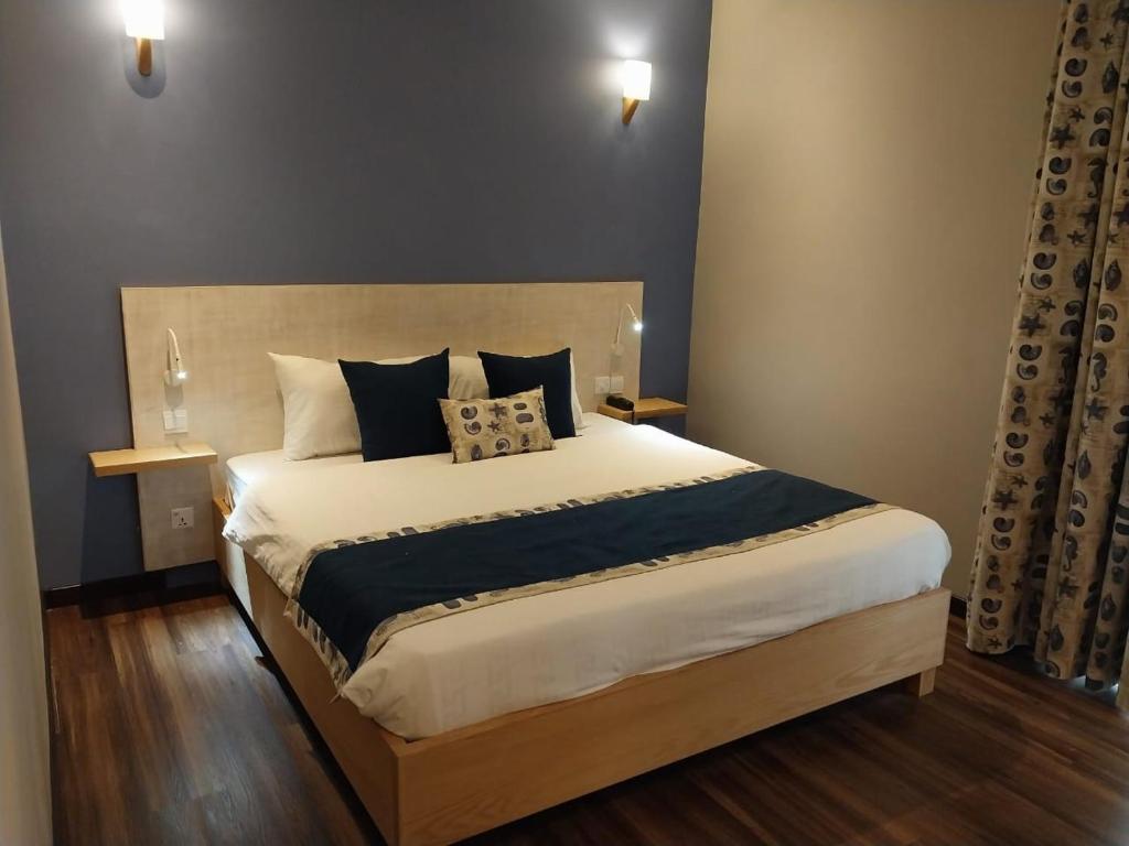 Mūsdienīgs guļamistabas interjers ar lielu gultu, tumši zilu sienu un elegantām gaismas ķermeņiem. Gultas veļa ir baltā krāsā ar tumši zilu akcentu.