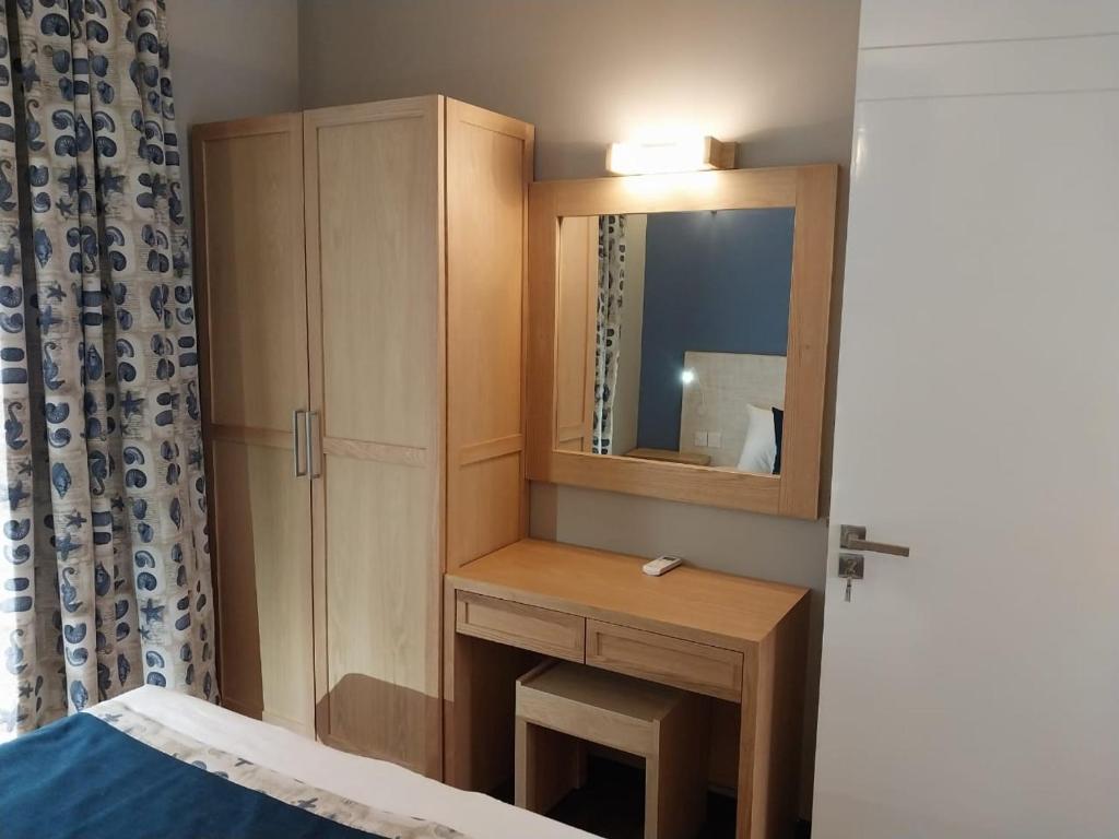 Mūsdienīgs guļamistabas stūris ar koka mēbelēm, ieskaitot skapīti un grieztiņu ar spoguli. Aiz loga redzamas ziloņu un jūras dzīvnieku motīvi uz aizkaru auduma.