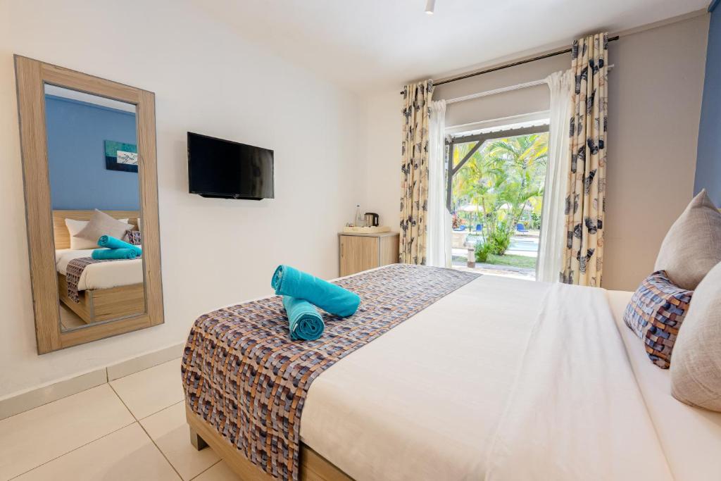 Mūsdienīga viesnīcas numuriņa iekārtojums ar gultu, televizoru un lielu spoguli. Numurā ir arī zili dvieļi un skats uz dārzu.