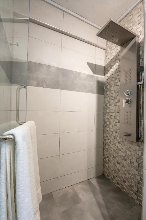 Mūsdienīga dušas telpa ar stikla durvīm un akmens flīzēm. Dušas galva un vadības panelis ir novietoti uz sienas.