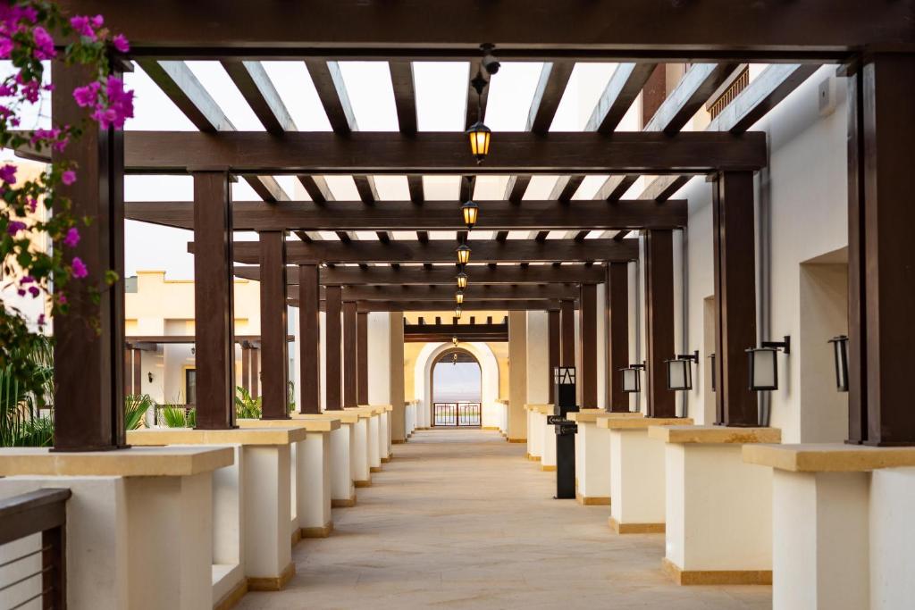 Eleganta terases gaitene ar koka siju konstrukciju un dekoratīvām laternām. Gaitenes malās redzami balti mūri un ziedošas puķes, radot relaksējošu atmosfēru.