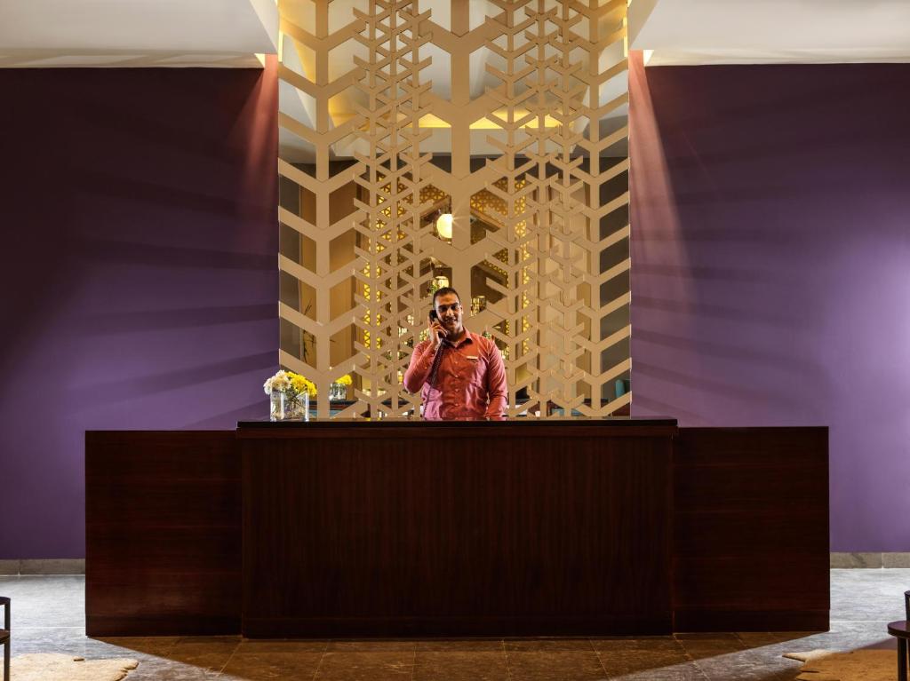 Recepcijas zona ar stilīgu dizainu, kur darbinieks runā pa telefonu. Fons ir violetās krāsas ar mūsdienīgu dekoratīvo elementu.