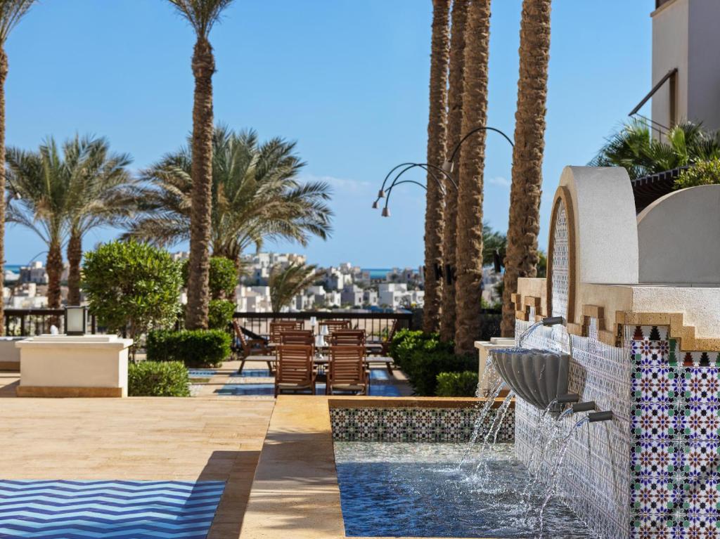 Luksusa viesnīcas dārza skats ar palmām, ūdens strūklaku un pludmales krēsliem, kas aicina uz atpūtu. Skats uz pilsētu un jūru.