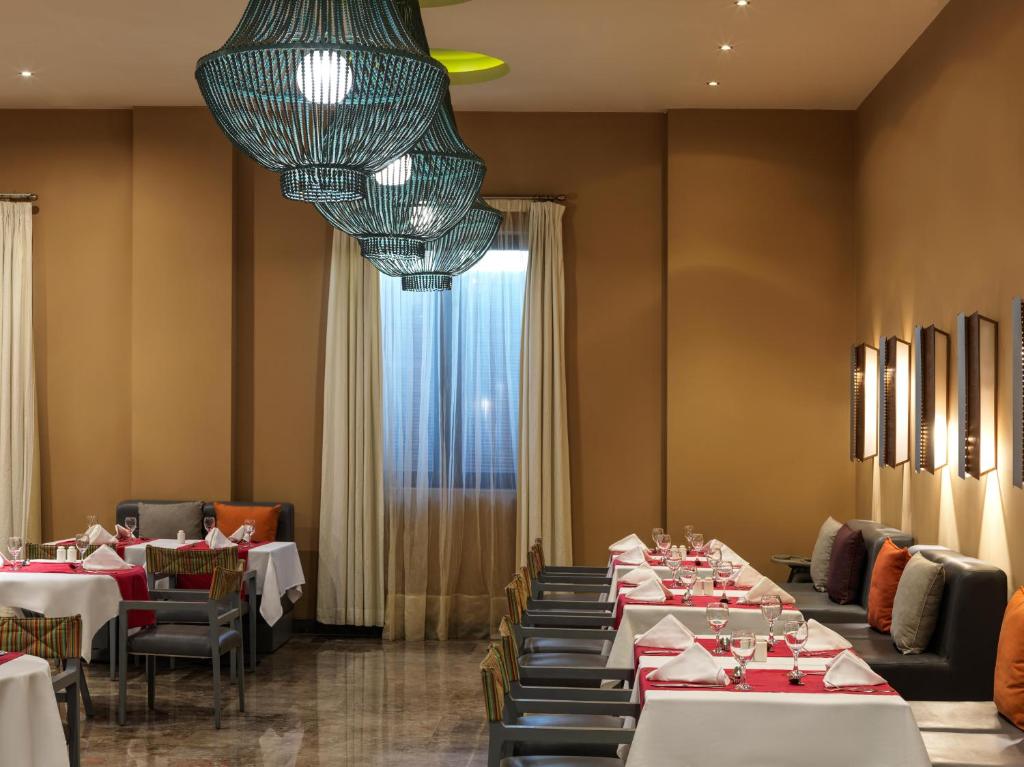 Mūsdienīgs restorāna interjers ar elegantiem galdiem, spilgtiem apgaismojumiem un komfortablām sēdvietām, radot siltu un viesmīlīgu atmosfēru.