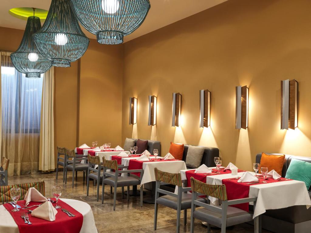 Elegants restorāna interjers ar krāsainām lampām un galdiem, kas klāti ar baltām un sarkanām galdautām. Siltas krāsas un mūsdienīgs dizains radījuši patīkamu atmosfēru.