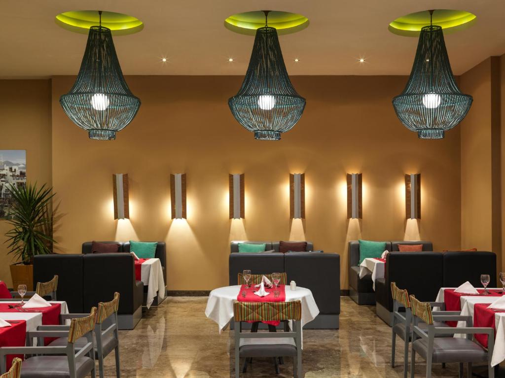 Mūsdienīgs restorāna interjers ar elegantiem lampām un komfortablām sēdvietām, nodrošinot patīkamu atmosfēru maltītēm. Sarkanās un baltās galdautas piešķir krāsu un dzīvīgumu telpai.