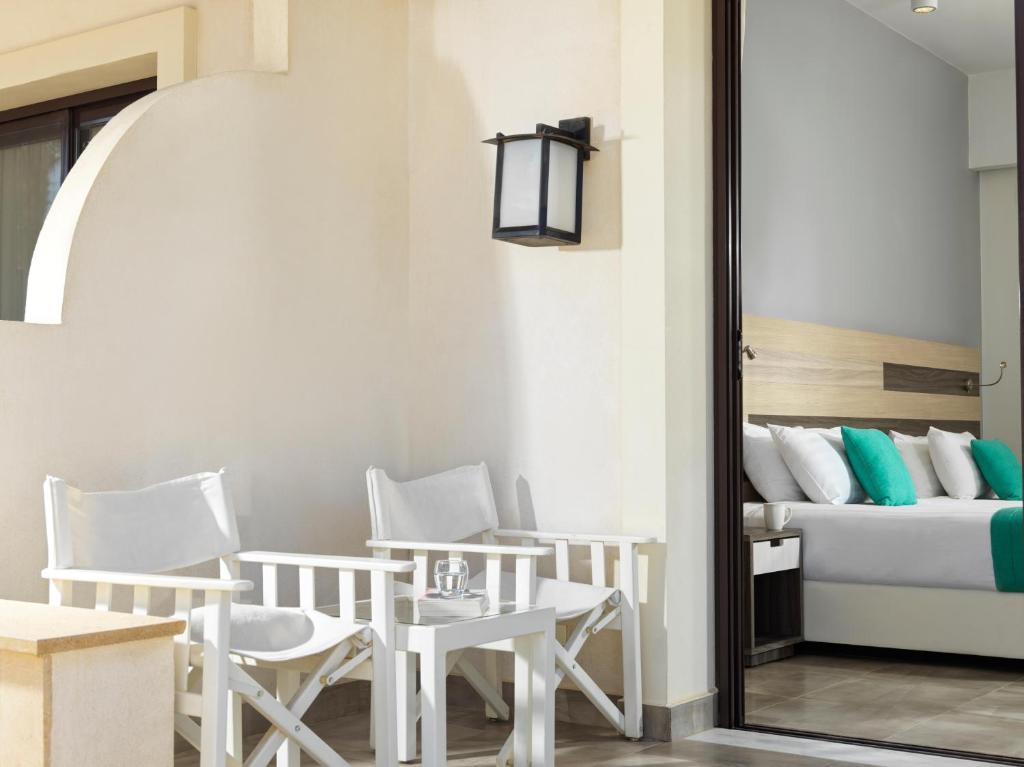 Terase ar baltām krēsliem un galdiņu, kas skata uz guļamistabu, kurā ir gulta ar spilveniem. Gaismas elementi un mūsdienīgs dizains piešķir telpai eleganci.