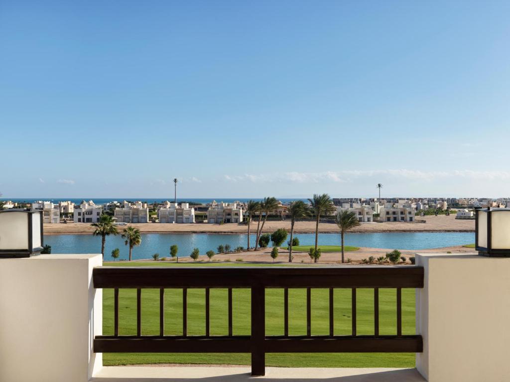 Skats no balkona uz piejūras ainavu ar modernām mājām, palmu kokiem un mierīgu ūdeni. Ideāla vieta atpūtai un relaksācijai, apvienojot dabu un mūsdienīgu arhitektūru.