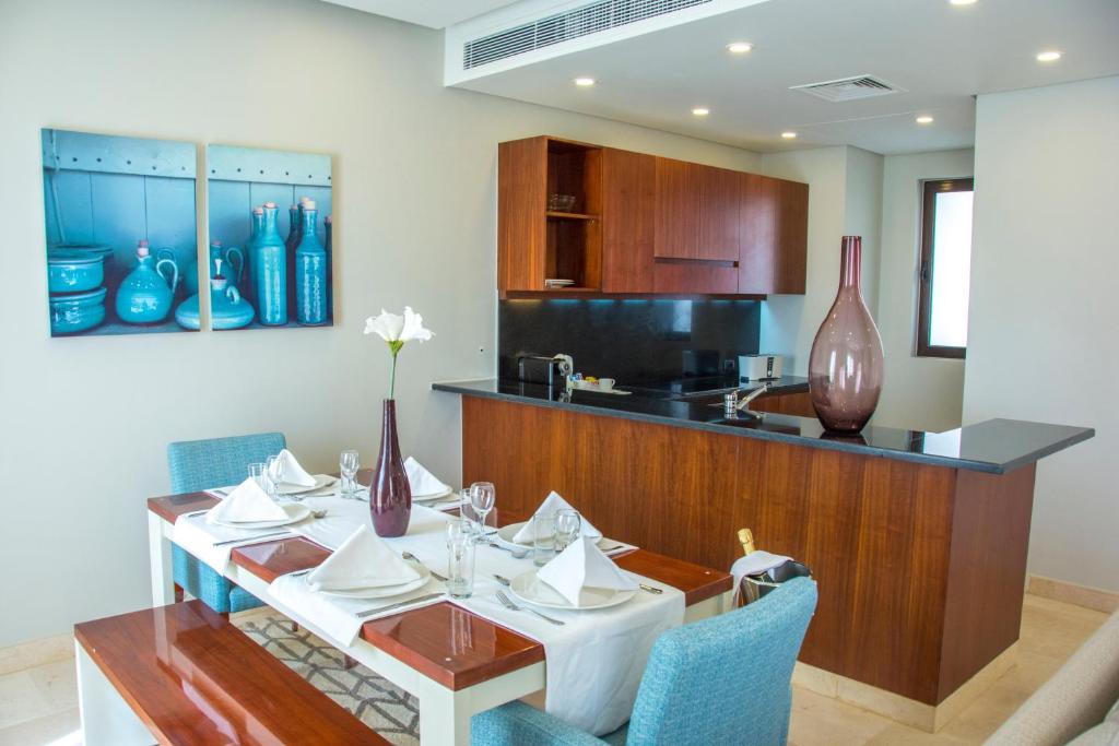 Mūsdienīga virtuve ar ēdamzonu, kurā ir eleganta galds ar galdautu un traukiem, kā arī stilīgas dekorācijas, tostarp vāze ar ziedu. Griestu apgaismojums un koka mēbeles rada siltu atmosfēru.