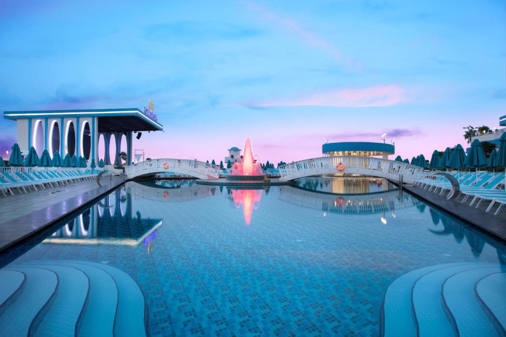 Mūsdienīgs peldbaseins ar tiltu un atsvaidzinošu strūklaku, apgaismots ar rozā un zilo nokrāsu, radot relaksējošu atmosfēru. Ap baseinu izvietotas sauļošanās krēsli.