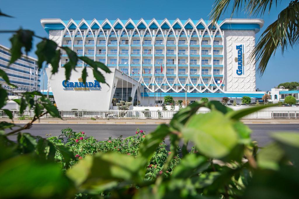 Granada viesnīca ar modernu arhitektūru un skaidru debesu fonu, ieskauta zaļiem augiem. Ideāla vieta atpūtai un brīvdienām.
