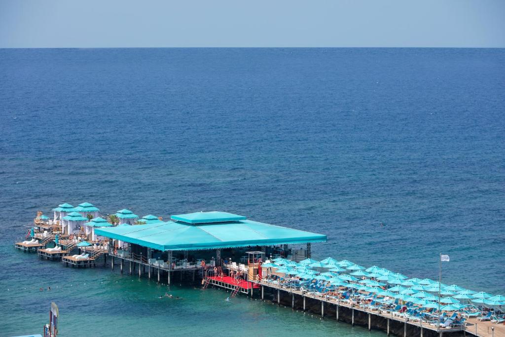 Pludmales bārs ar zilajiem saulessargiem un atpūtas krēsliem, kas izvietoti pie jūras. Skats uz mierīgu, zilu ūdeni un debesi.