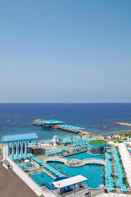 Vasaras kūrorts ar zilām peldbaseina zonām un pludmales sauļošanās vietām, kas atrodas pie krasta. Skats uz jūru un piestātni ar atpūtas zonām.