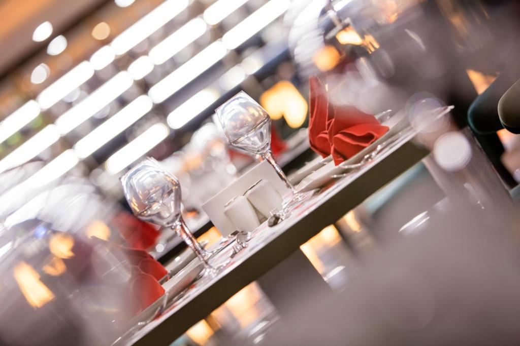 Elegants restorāna galdiņš ar sarkaniem salvešiem un glāzēm, radot patīkamu atmosfēru. Fons ar mīkstām gaismām piešķir siltu noskaņu.