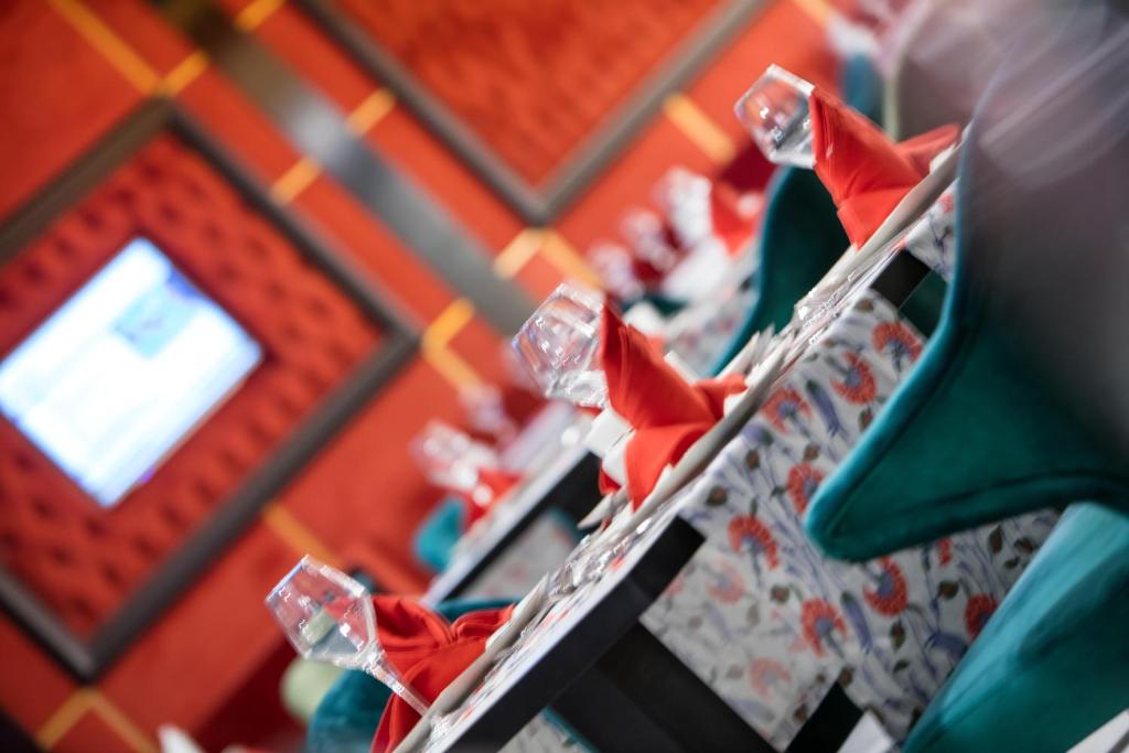 Elegants restorāna interjers ar galdiem, kas klāti ar krāsainām salvētēm un glāzēm, radot viesmīlīgu atmosfēru. Sarkanā un zaļā krāsa piešķir dzīvīgumu un komfortu.